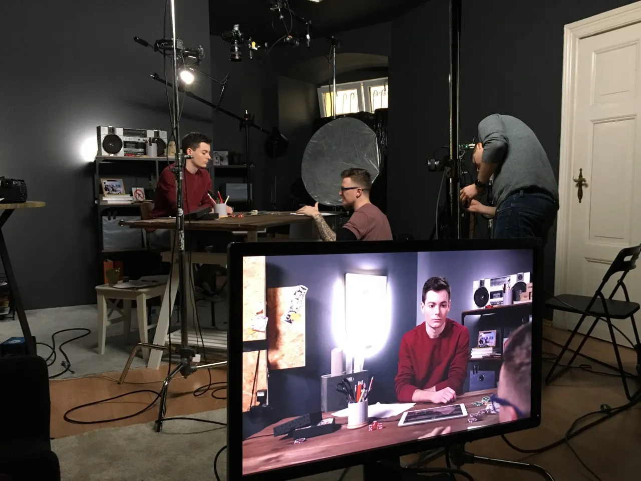 Luke Hunter on set at a table, with the camera crew and a monitor showing his performance