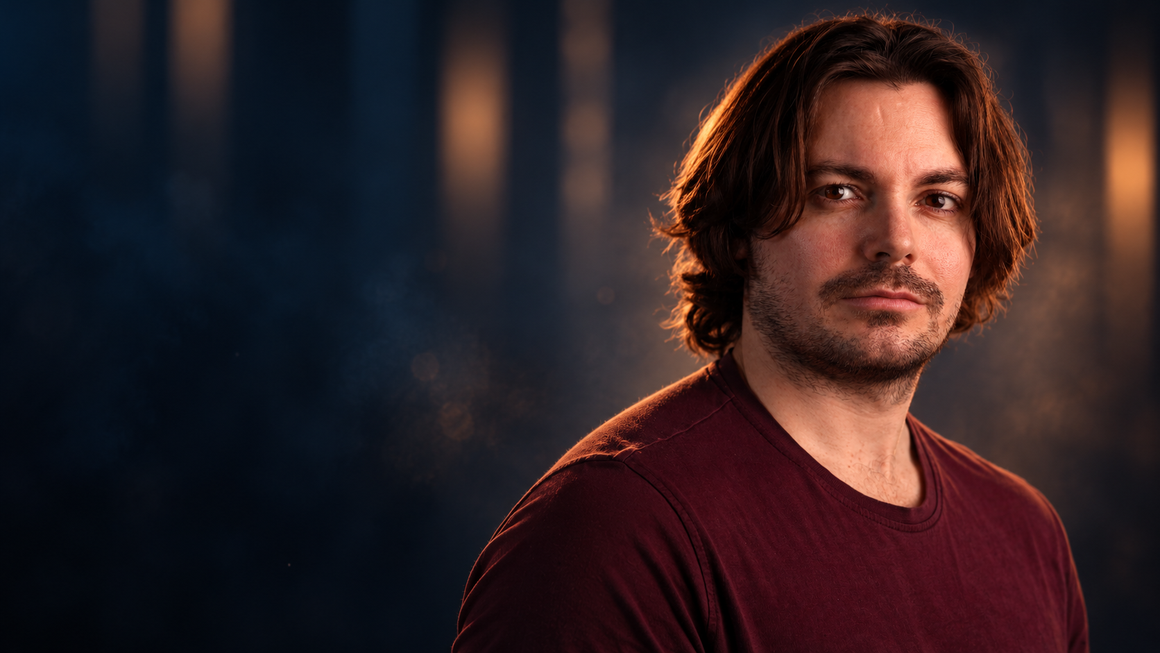 Luke Hunter in a burgundy shirt against a deep navy and warm amber background